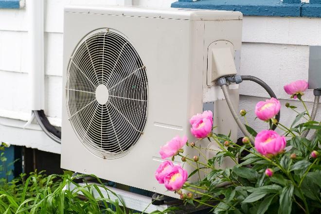 A typical heat pump, consisting of a boxy white frame similar to an air conditioning unit, is pictured on the side of a home.