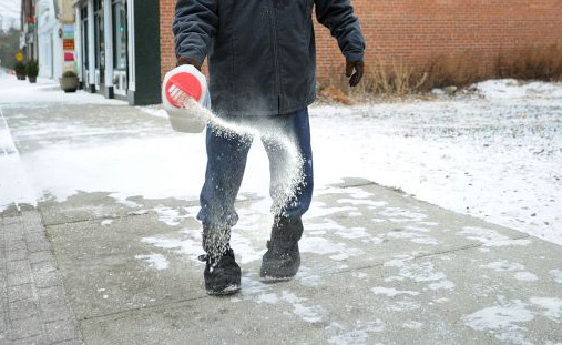 Man spreads de-icer on an icy sidewalk