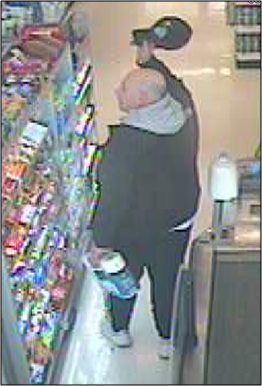 Suspect is seen at checkout, appearing to be light-skinned, bald, and heavyset, wearing black athletic pants, black jacket over gray hoodie, and a black ball cap.